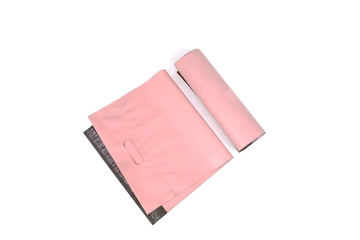 Pink handled poly mailer laid flat next to a rolled one, showing the die-cut handle and seal strip