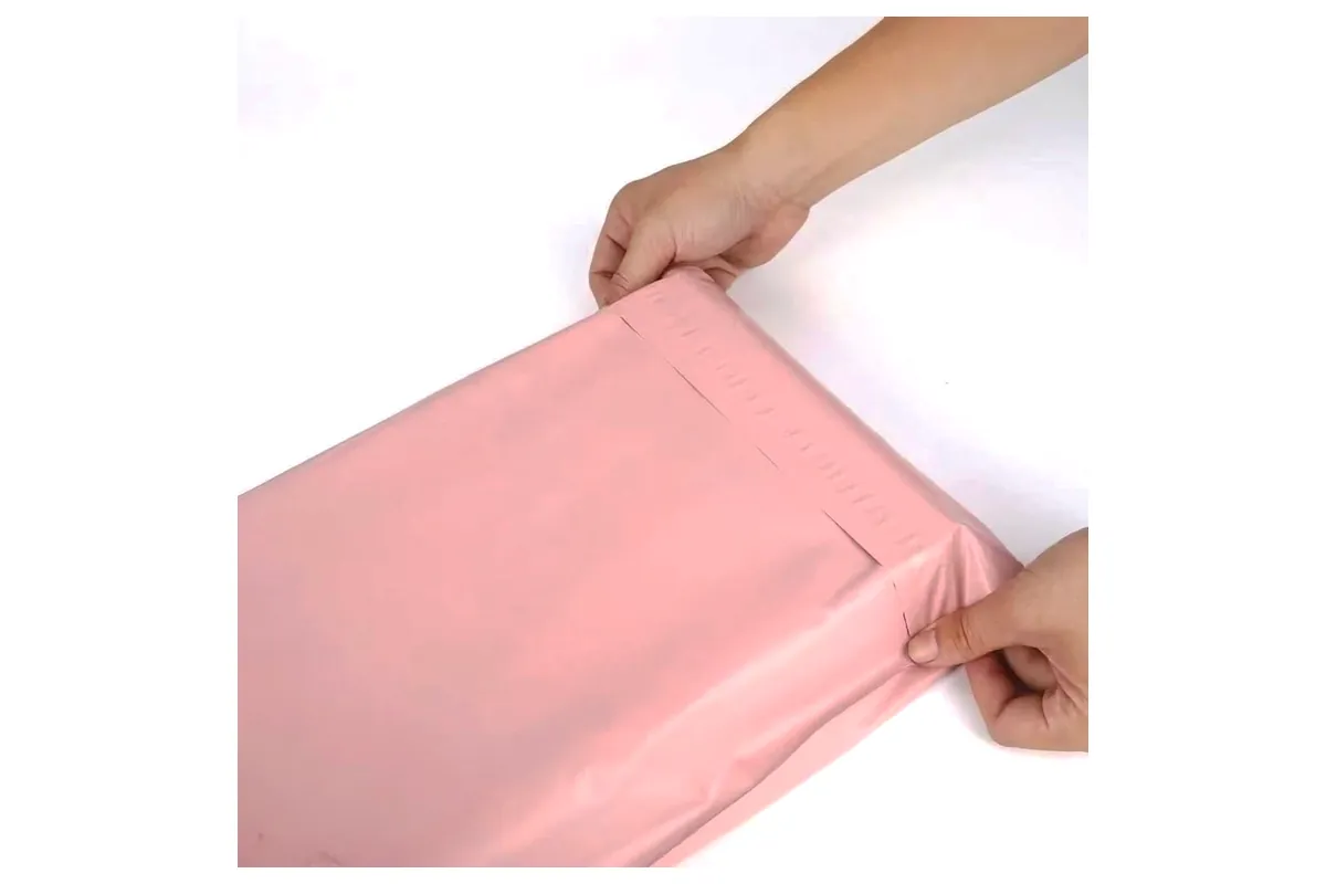 Hands pressing the self-seal adhesive strip closed on a pink poly mailer