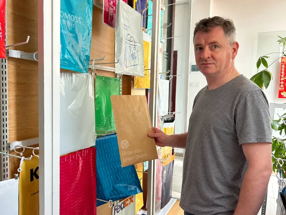 Noel, co-owner, at the sample wall of printed mailers in Dongguan